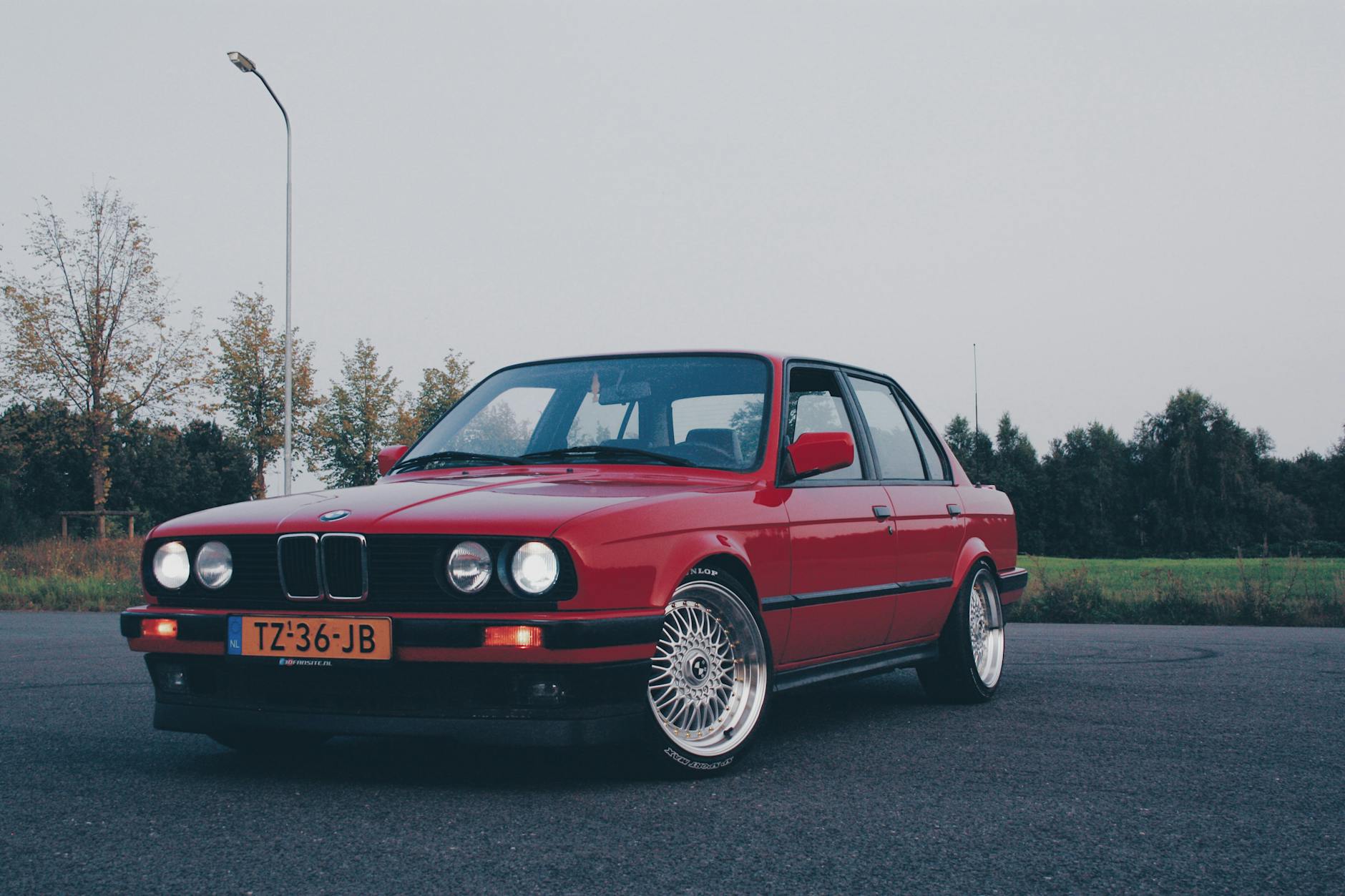 Classic Red BMW E30 garé à l'extérieur, présentant son style vintage et ses fonctionnalités chromées.
