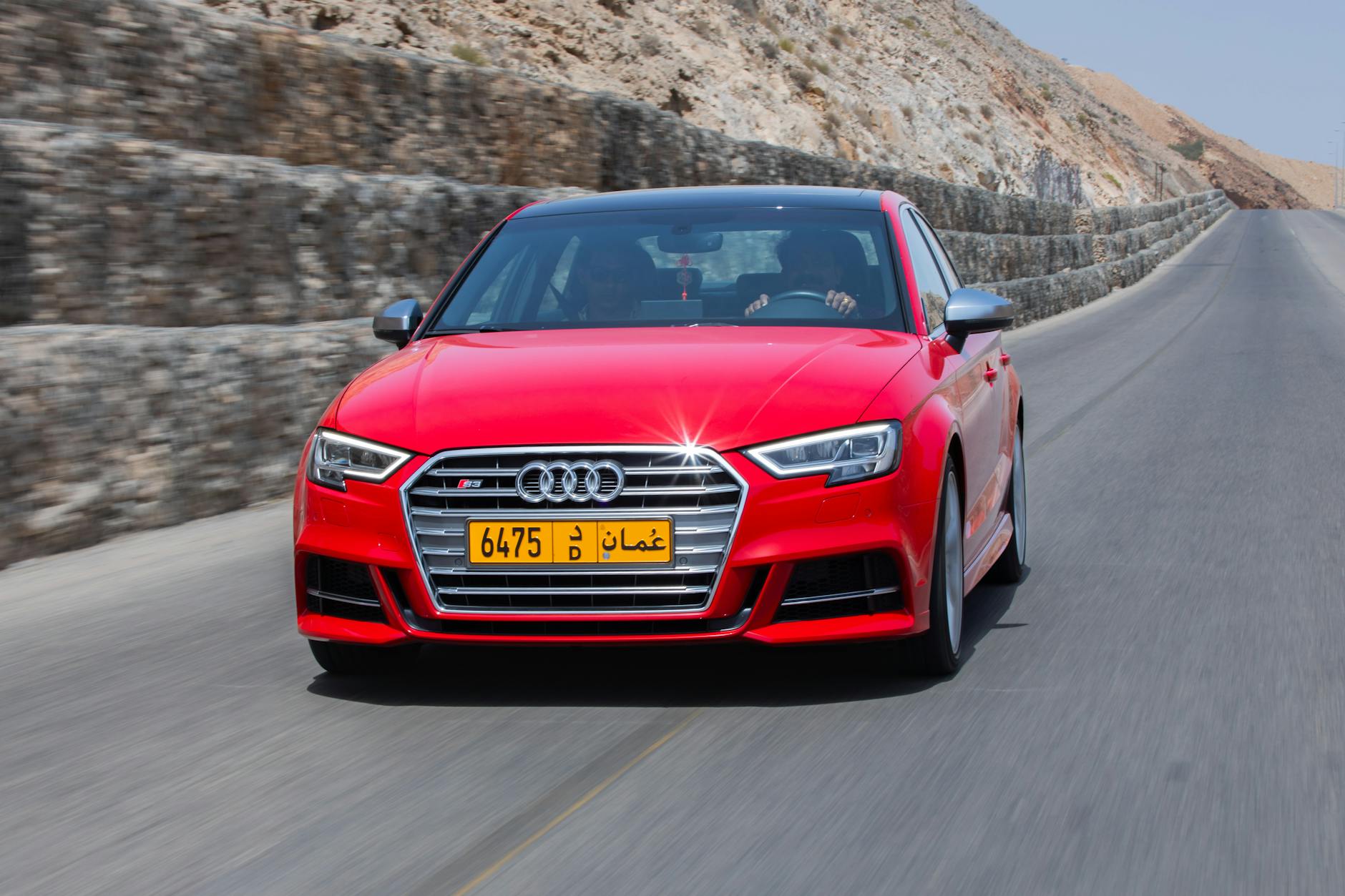 Une Audi S3 rouge vibrante le long d'une route de montagne pittoresque sous un ciel clair à Oman.