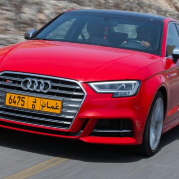 Voiture rouge dynamique sur une route panoramique à Muscat, Oman, présentant le design et la vitesse modernes.