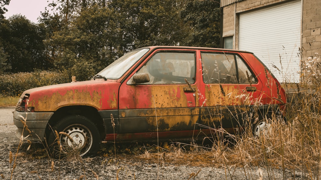 Une voiture rouillée assise dans un champ à côté d'un bâtiment