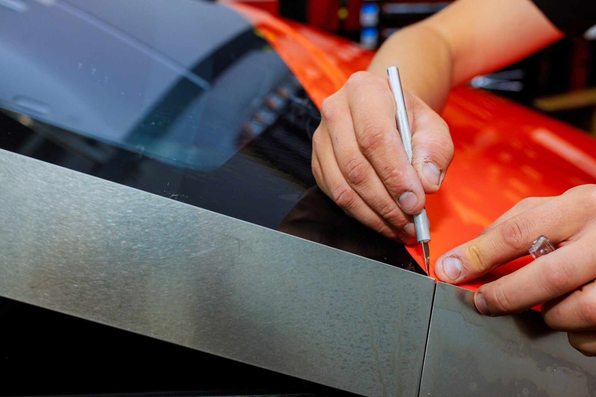 Le travailleur du technicien se concentre sur la précision tout en coupant un film de vinyle orange à la voiture pour protéger l'automobile du corps