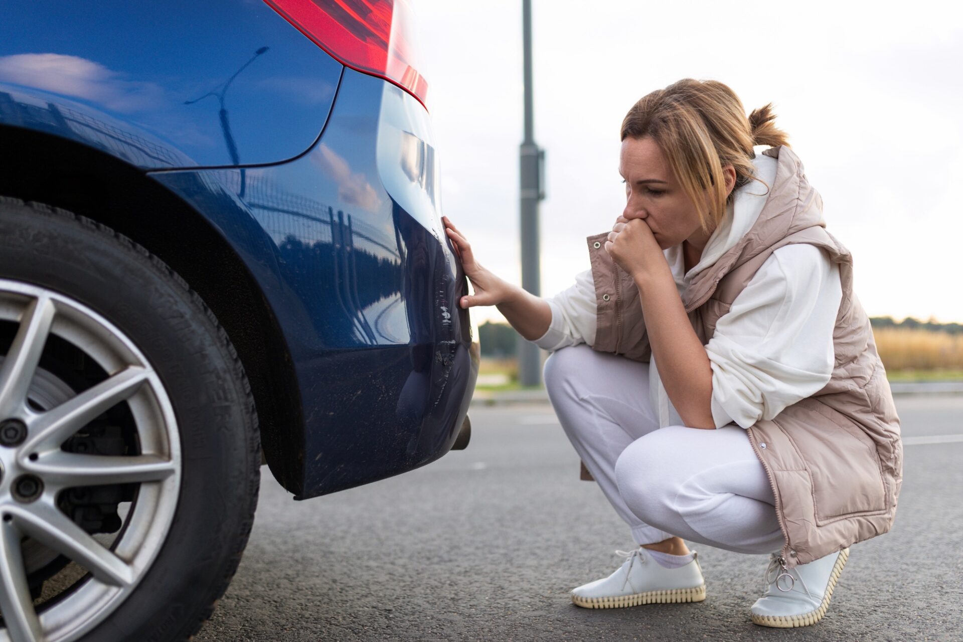 Femme perplexe et agacée qui regarde à zéro sur le pare-chocs de voiture après un accident mineur.