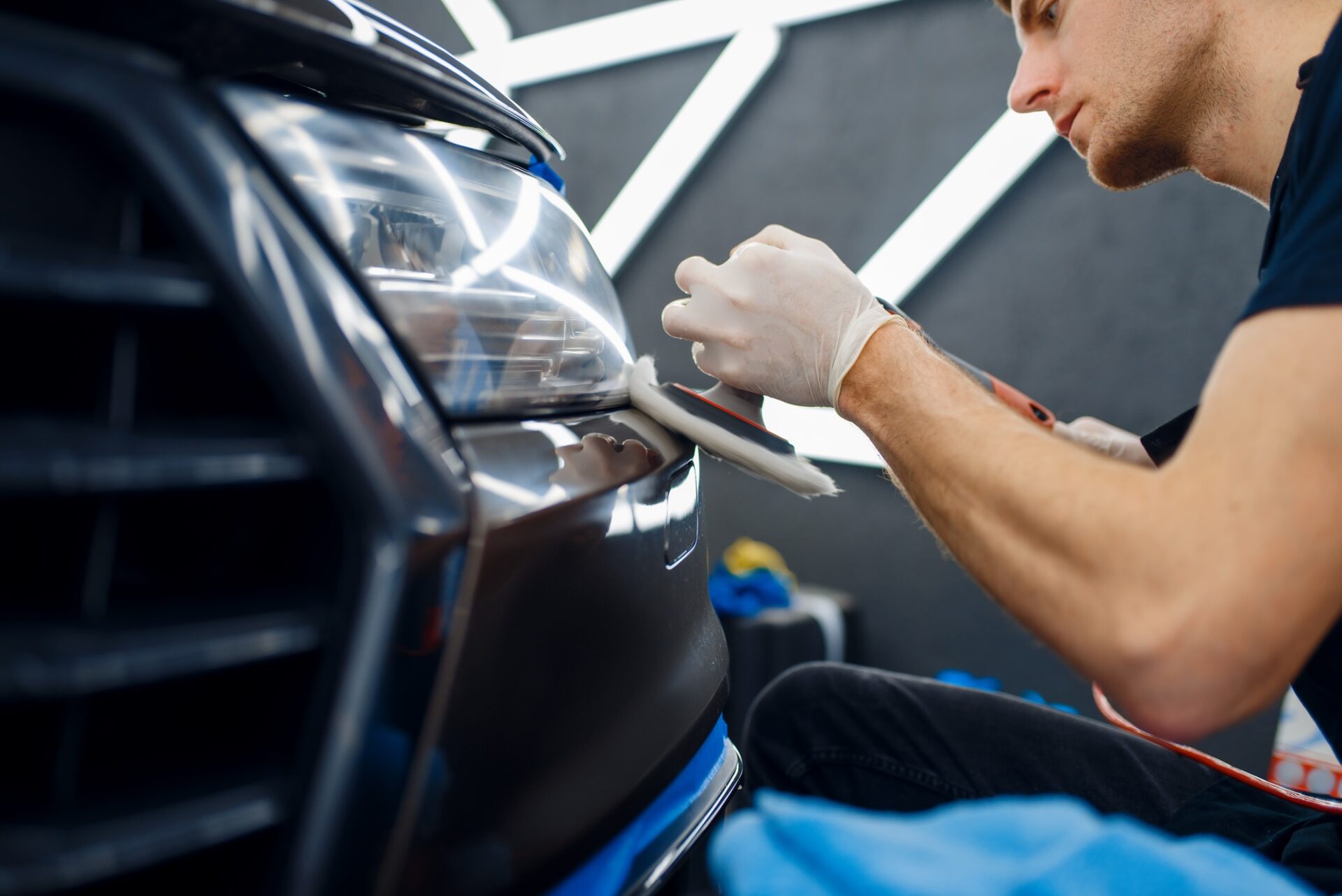 Le travailleur masculin polir le pare-chocs avant à l'aide de la machine de polissage, la voiture détaillant le gros plan. 