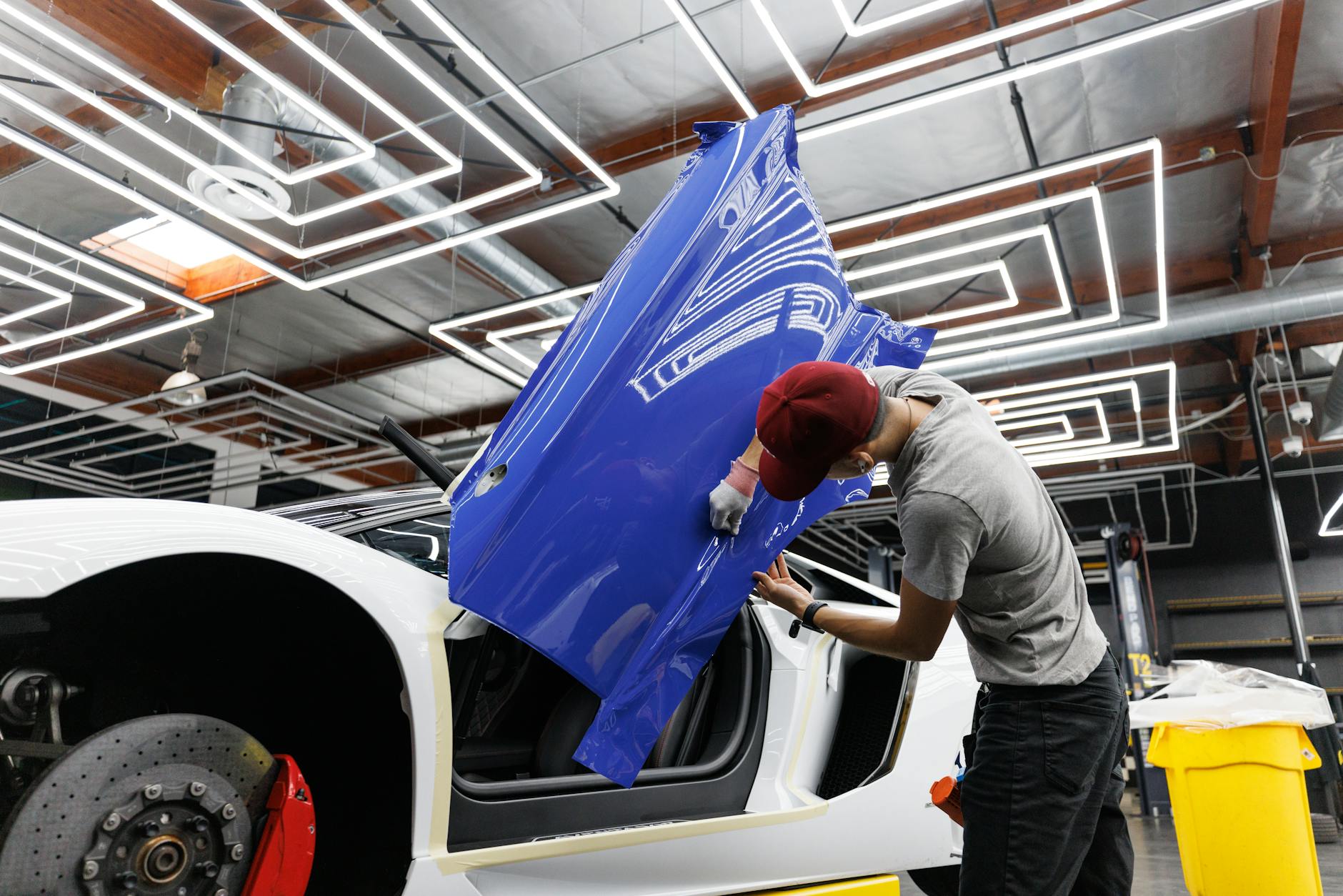 Mécanique automatique appliquant une enveloppe en vinyle bleu sur une porte de voiture dans un garage moderne.