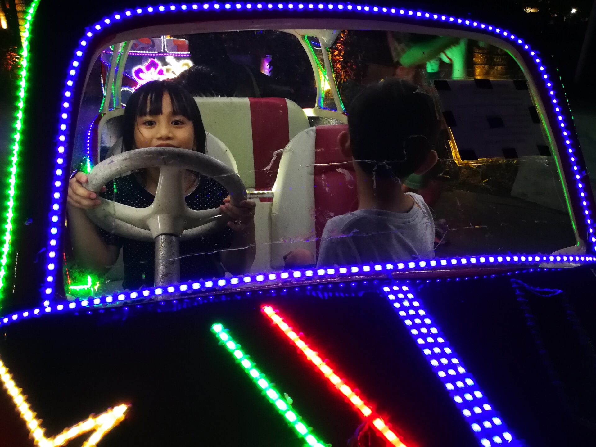 Enfant conduisant une voiture néon la nuit dans le parc d'attractions