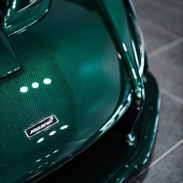 Hotte de supercar vert foncé avec texture en fibre de carbone dans une salle d'exposition.