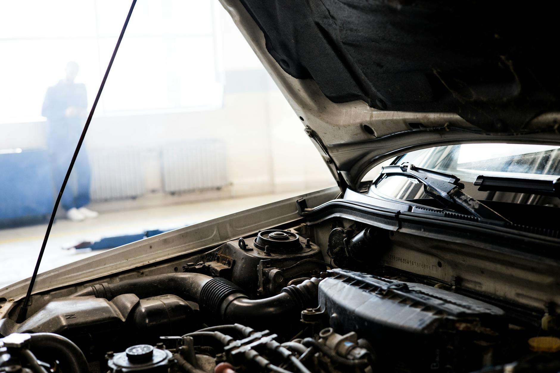 Image détaillée d'un moteur de voiture sous le capot ouvert dans un garage intérieur bien éclairé.