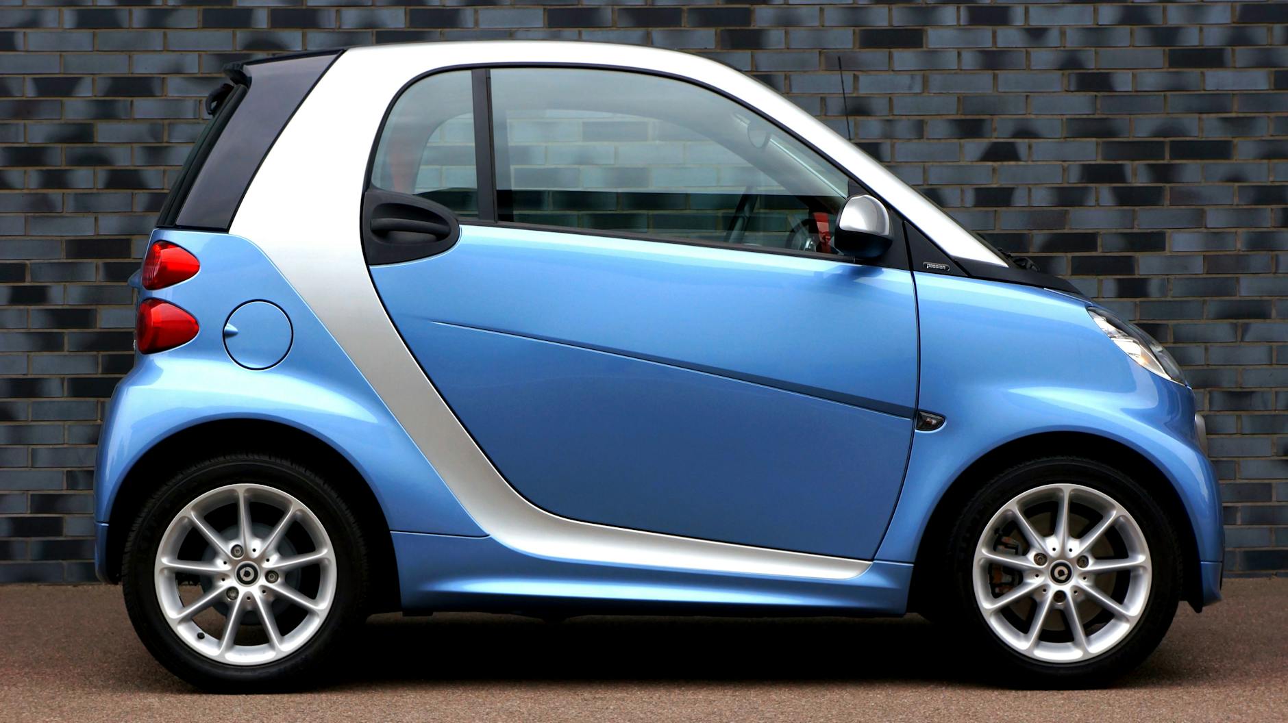 Vue latérale d'une voiture intelligente bleue moderne contre un mur de briques, présentant un design compact.