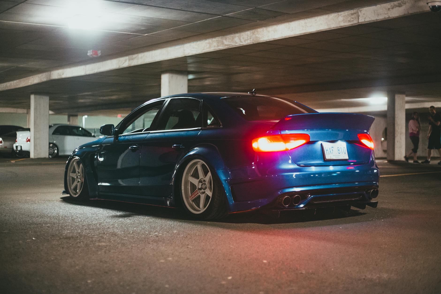Une berline bleue élégante modifiée dans un parking souterrain, présentant une suspension abaissée et des roues personnalisées.