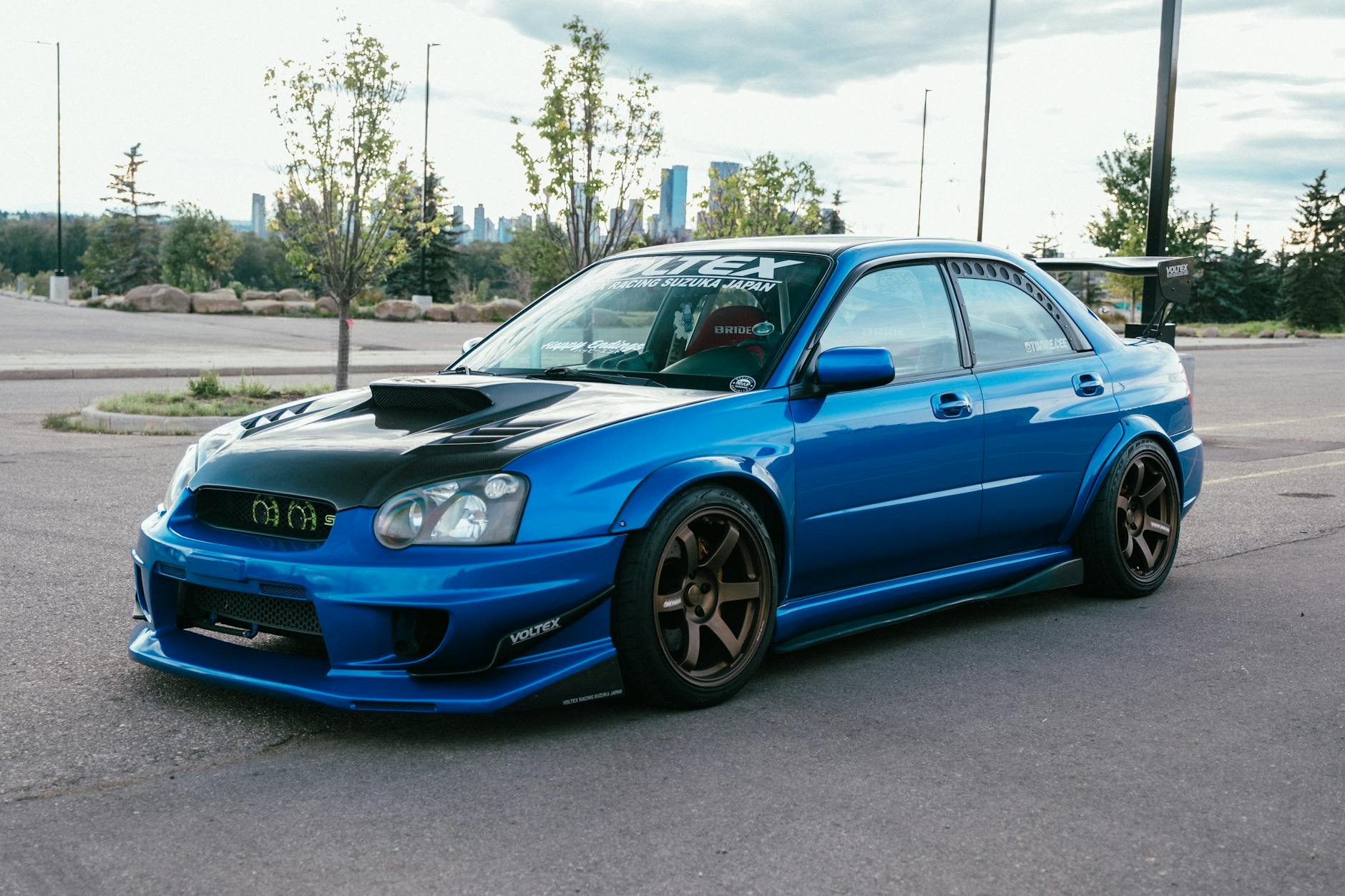 Une Subaru Sti bleue élégante et modifiée s'est garée à l'extérieur avec une vue sur les toits de la ville.