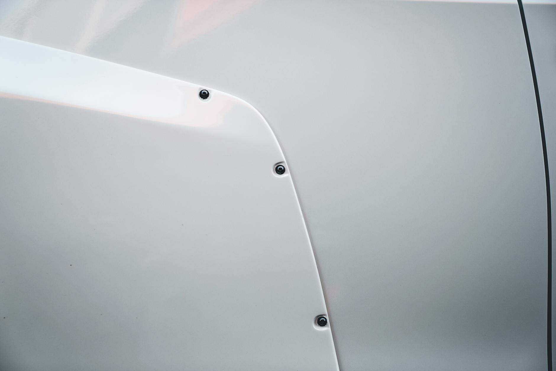 Vue détaillée d'un panneau de voiture blanc mettant en évidence les vis et les textures lisses.