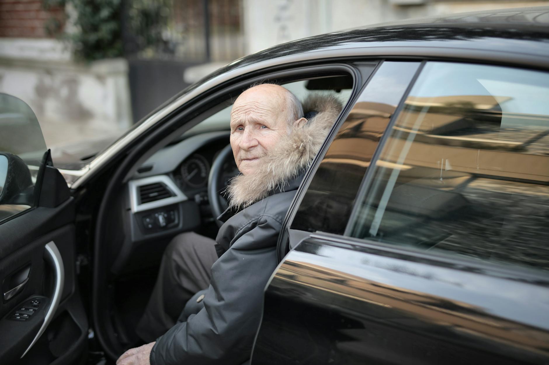 Un homme âgé dans un manteau d'hiver sortant d'une voiture garée à l'extérieur.
