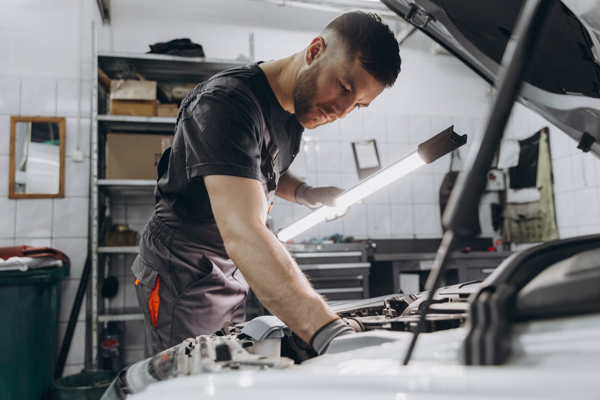 Concept de service, de réparation, d'entretien et de personnes - Mécanicien de voiture avec la lampe travaillant à l'atelier
