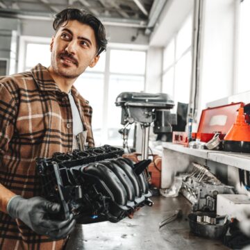 part-car Jeune homme mécanicien réparant les pièces de voiture sur la table de travail dans l'atelier de service de voiture