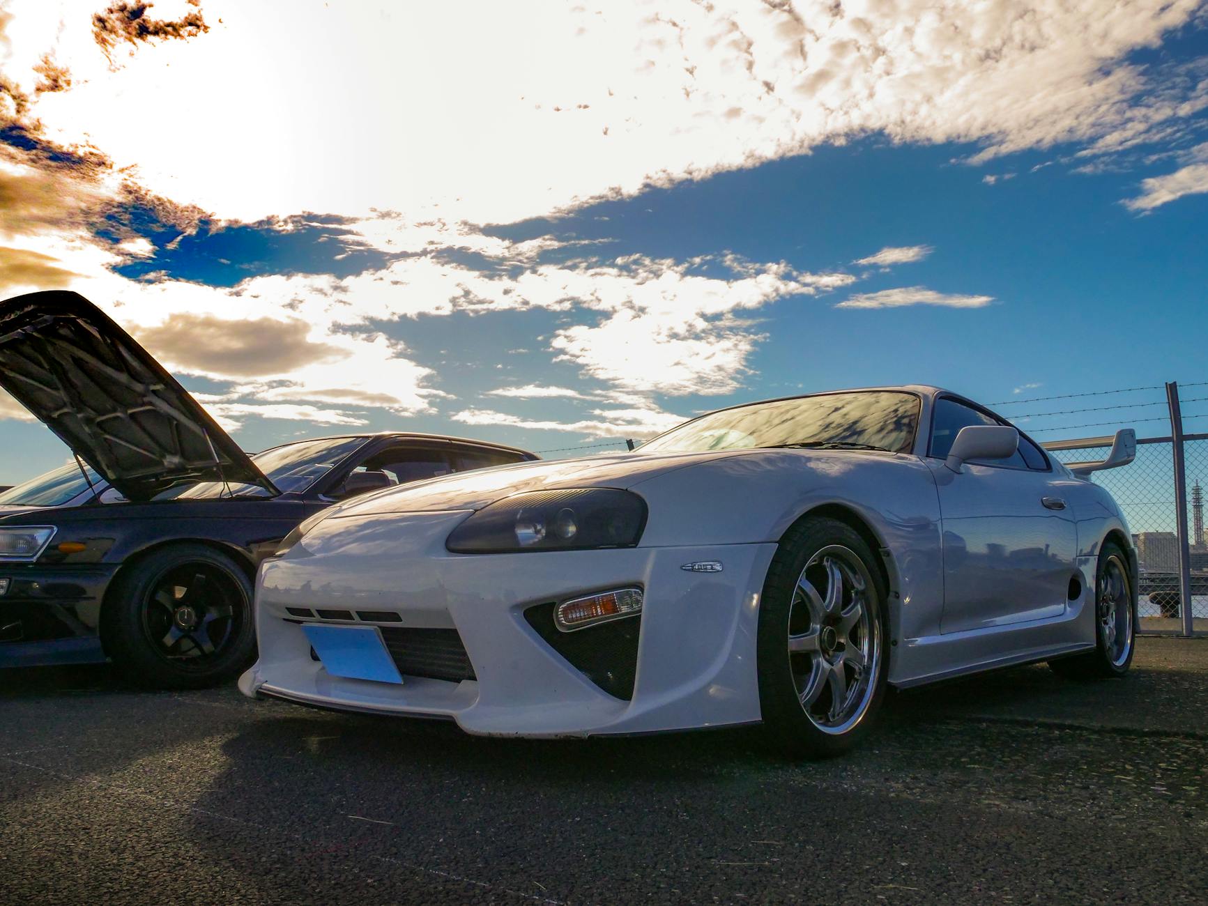 Photo captivante de la culture JDM mettant en vedette une Toyota Supra lors d'une réunion de voiture dynamique sous un ciel magnifique.