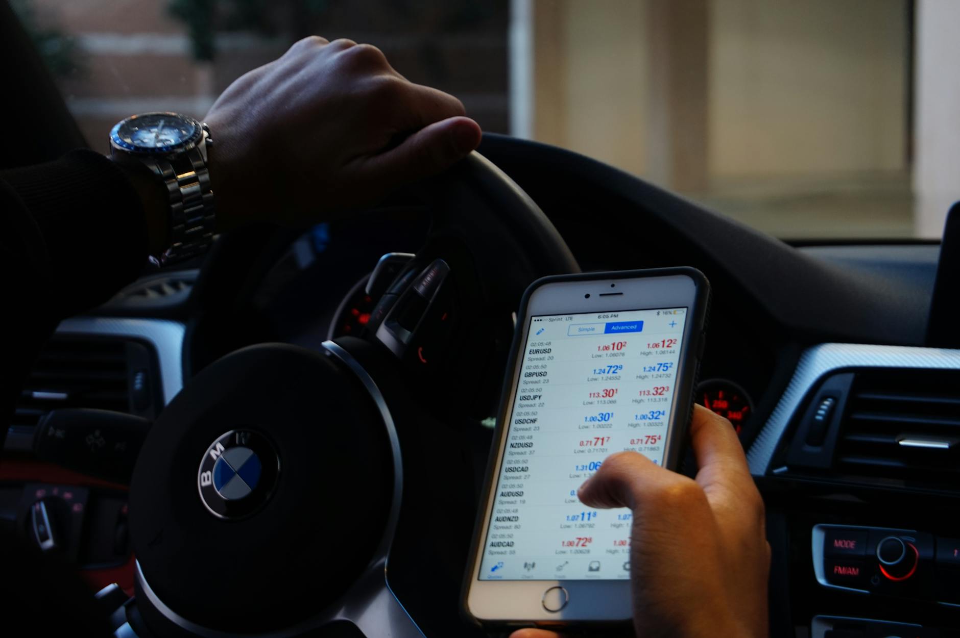 Personne utilisant un téléphone portable pour échanger des devises tout en conduisant une voiture BMW.