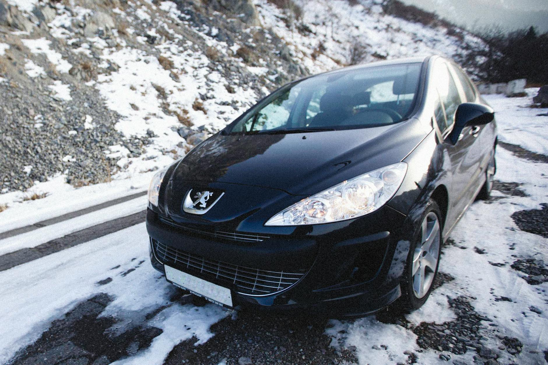 Une élégante voiture Peugeot garée sur une route de montagne enneigée en hiver, mettant en valeur le style et la nature.