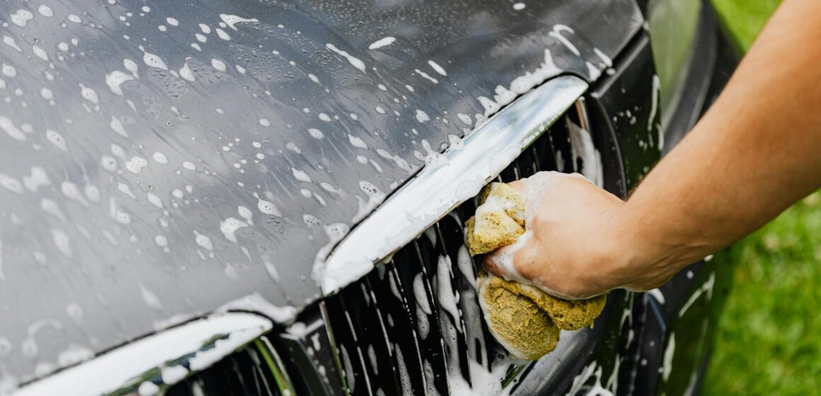 clean-car Vue détaillée d'une main lavant une calandre de voiture avec une éponge savonneuse à l'extérieur.