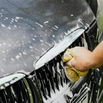 Vue détaillée d'une main lavant une calandre de voiture avec une éponge savonneuse à l'extérieur.
