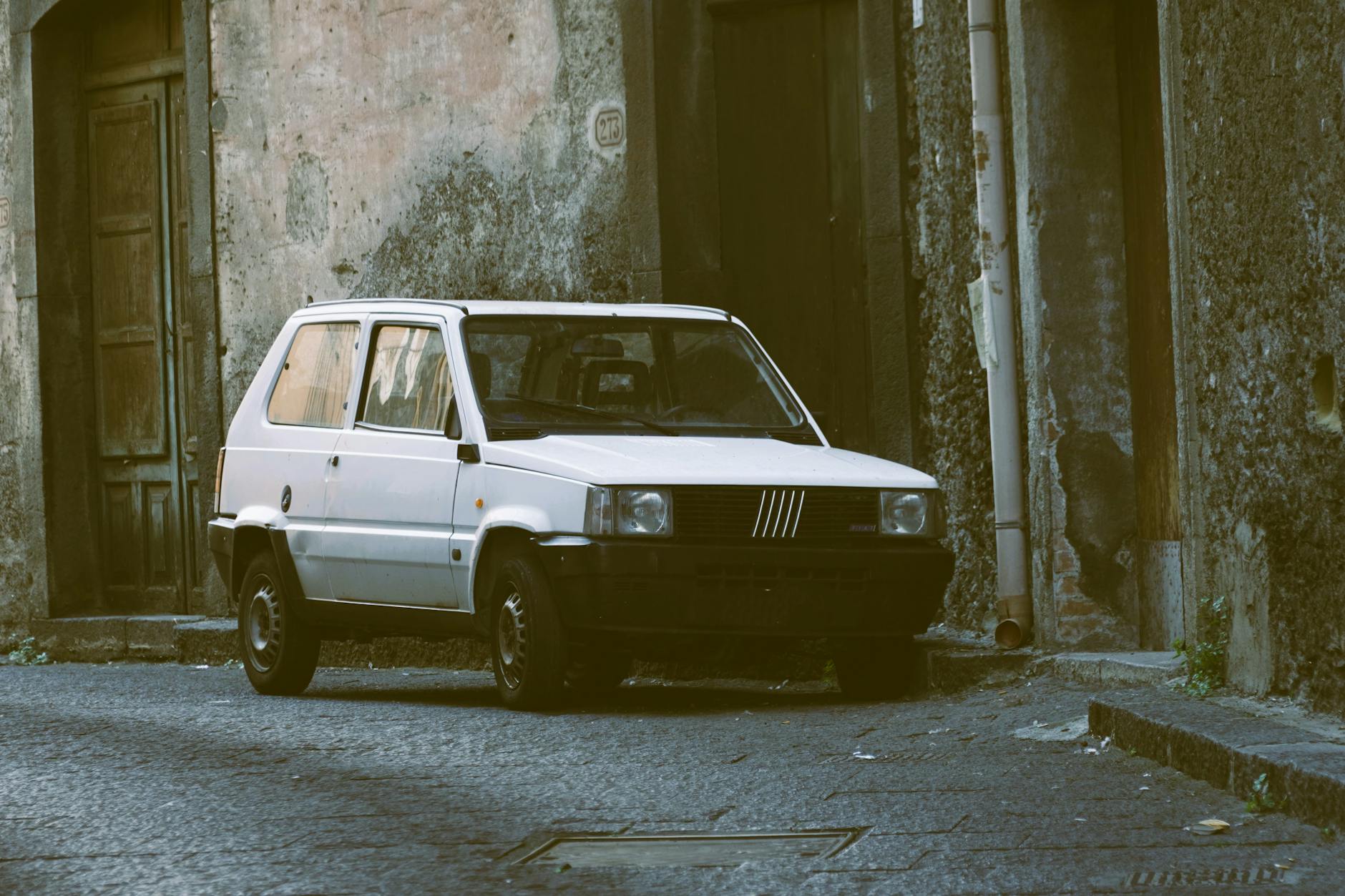 Une Fiat Panda blanche classique garée dans une ruelle urbaine étroite au charme vintage.