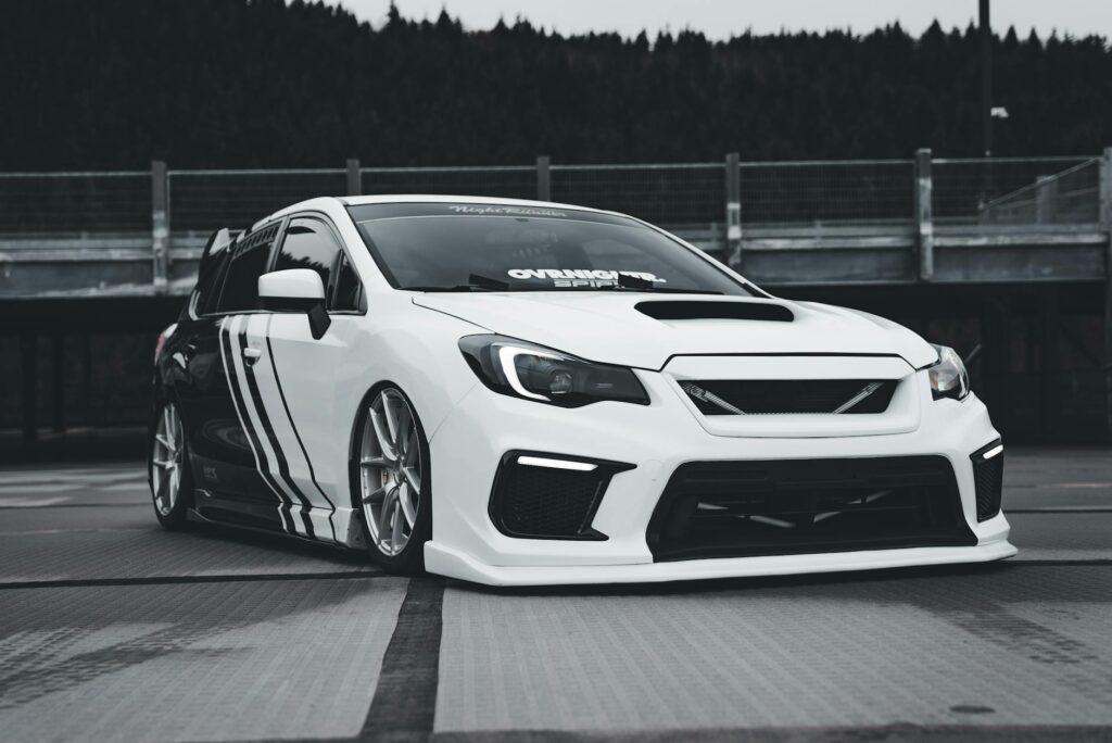 Subaru WRX blanche et élégante avec une livrée personnalisée dans un contexte urbain moderne, mettant en valeur le réglage des voitures de sport.