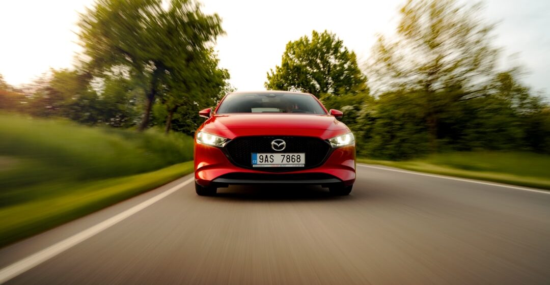 Mazda-3-BP une voiture rouge roulant sur une route avec des arbres en arrière-plan