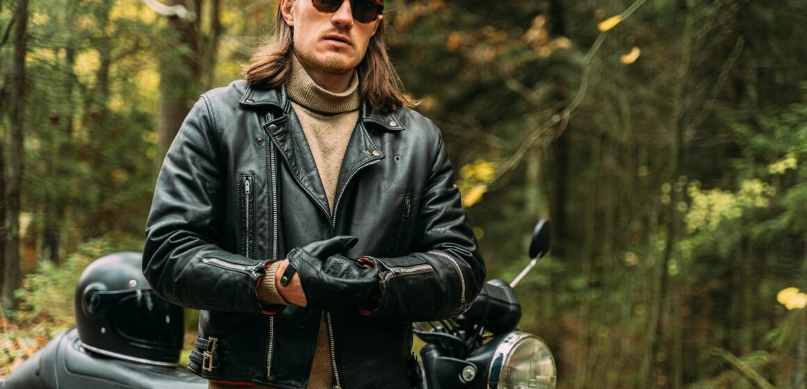 Style-biker Motard confiant en veste de cuir noir debout en moto dans un cadre forestier.
