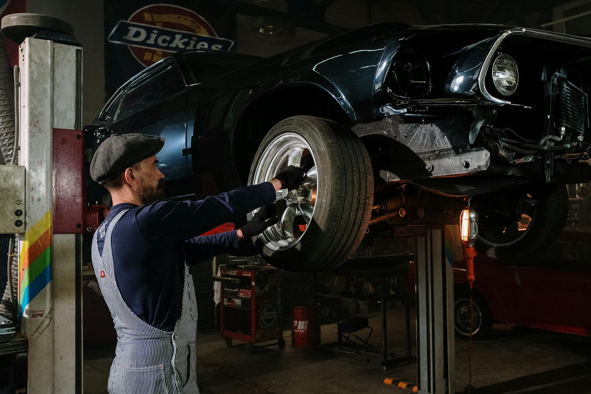 Un mécanicien concentré travaille sur une roue de voiture dans un garage faiblement éclairé, mettant en valeur ses compétences en réparation automobile.