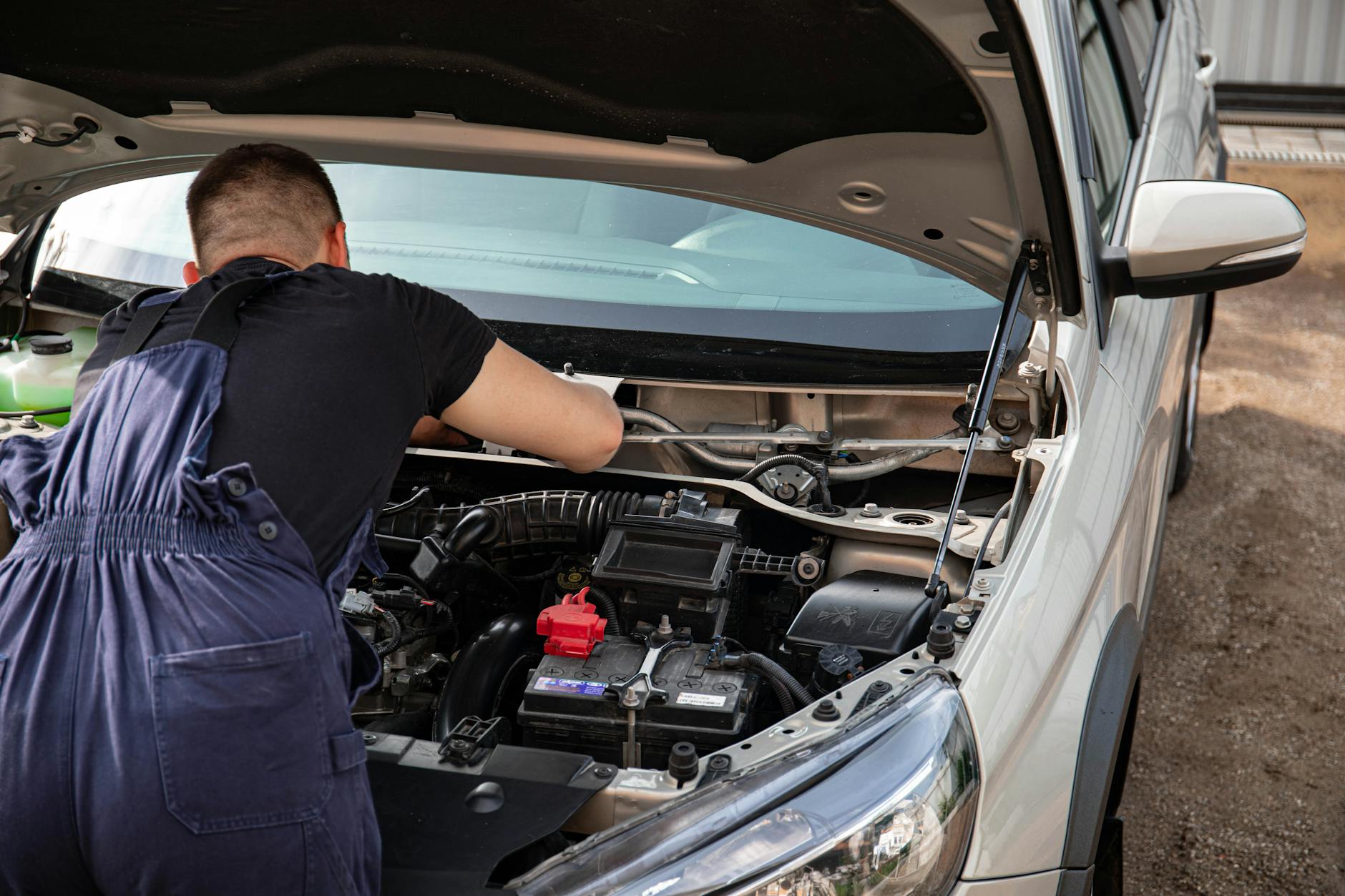 Un mécanicien répare un moteur de voiture à l'extérieur, en se concentrant sur l'entretien du véhicule.