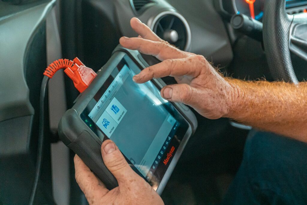 Mécanicien utilisant un outil de diagnostic à l'intérieur d'une voiture pour vérifier les problèmes de moteur et assurer un bon entretien.