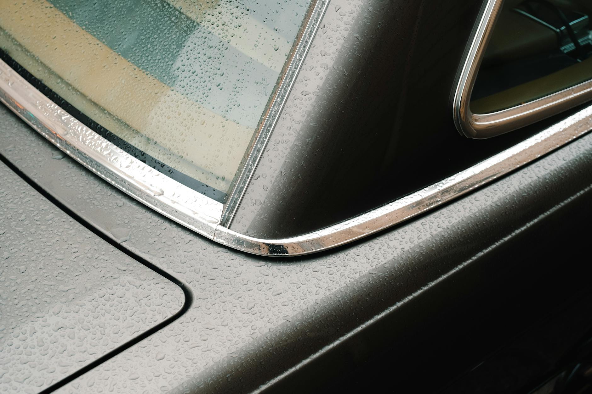 Vue détaillée de la surface mouillée d'une voiture ancienne avec des gouttes de pluie sur la fenêtre.